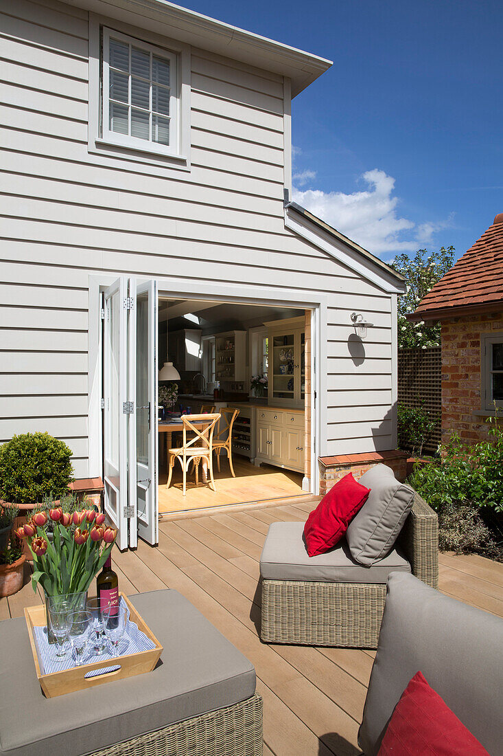 Red cushions and tulips with wicker furniture on decked exterior of Surrey home, England, UK