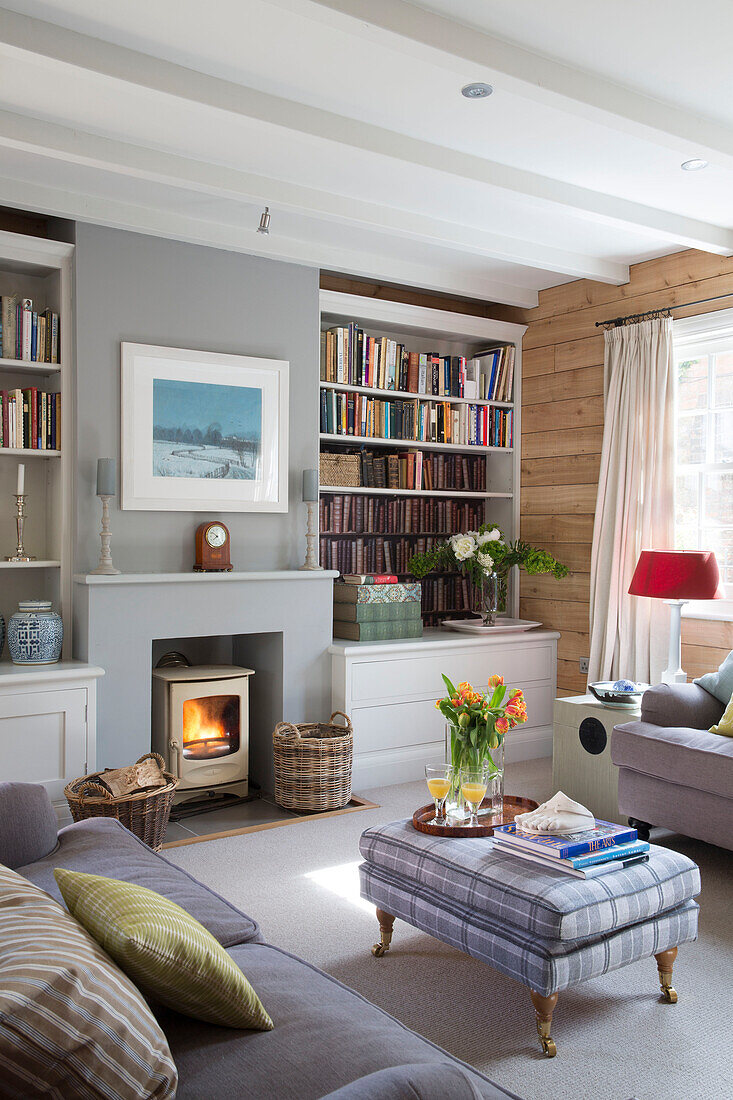 Hellgraue Sofas in holzgetäfeltem Wohnzimmer mit beleuchtetem Kamin in einem Haus in Surrey, England, UK