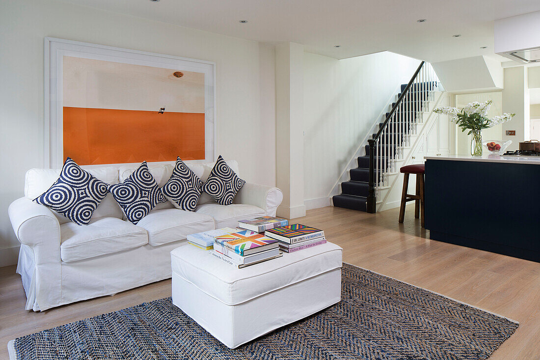 Books on ottoman with white sofa and modern artwork in open plan living room of London townhouse   England   UK