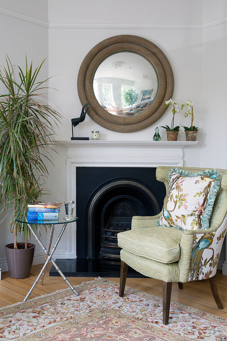 Light green armchair and circular mirror at fireside in London townhouse England UK