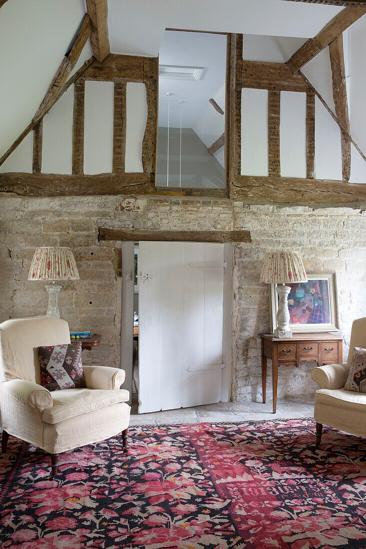 Pair of cream armchairs with pink floral rug in timber-framed Sussex country house England UK