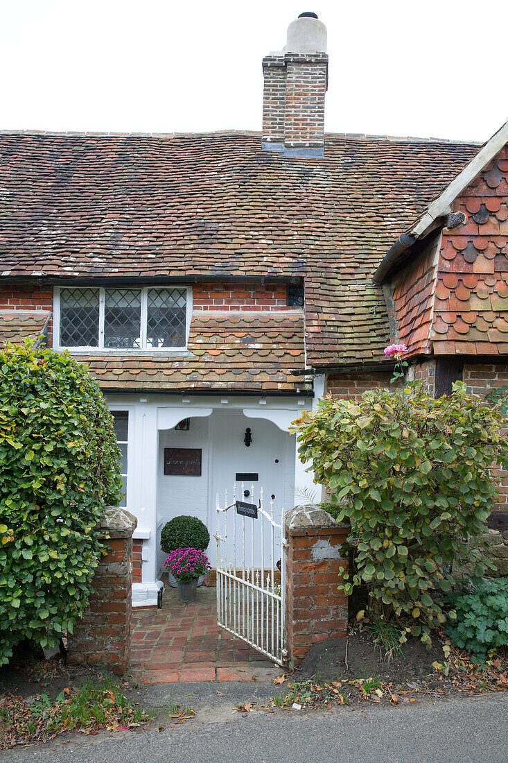 Open gate to white paintwork on front door of tiled Surrey cottage England UK