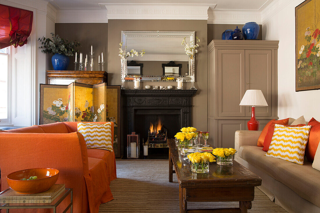 Gelbe Rosen auf hölzernem Couchtisch mit orangefarbenem Sofa in einem Londoner Stadthaus-Wohnzimmer UK