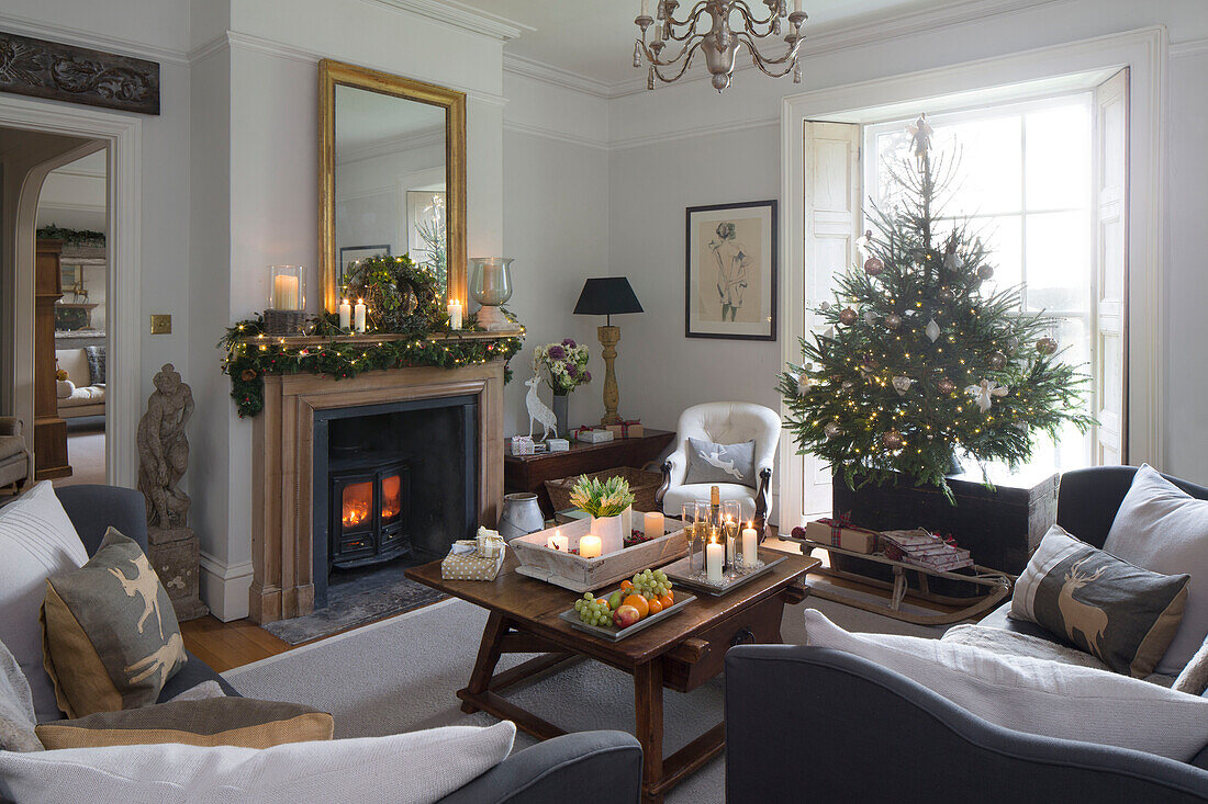 Angezündete Kerzen und Holzofen mit Weihnachtsbaum im Fenster eines Hauses in Surrey, England UK