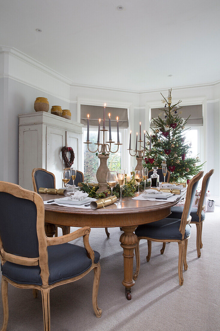 Lit candles on wooden table with Christmas tree in window of Surrey home England UK