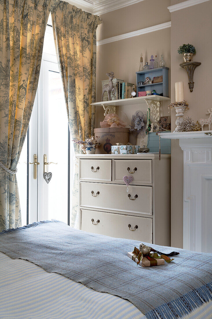 Trinkets on chest of drawers at double doors in bedroom of London home England UK