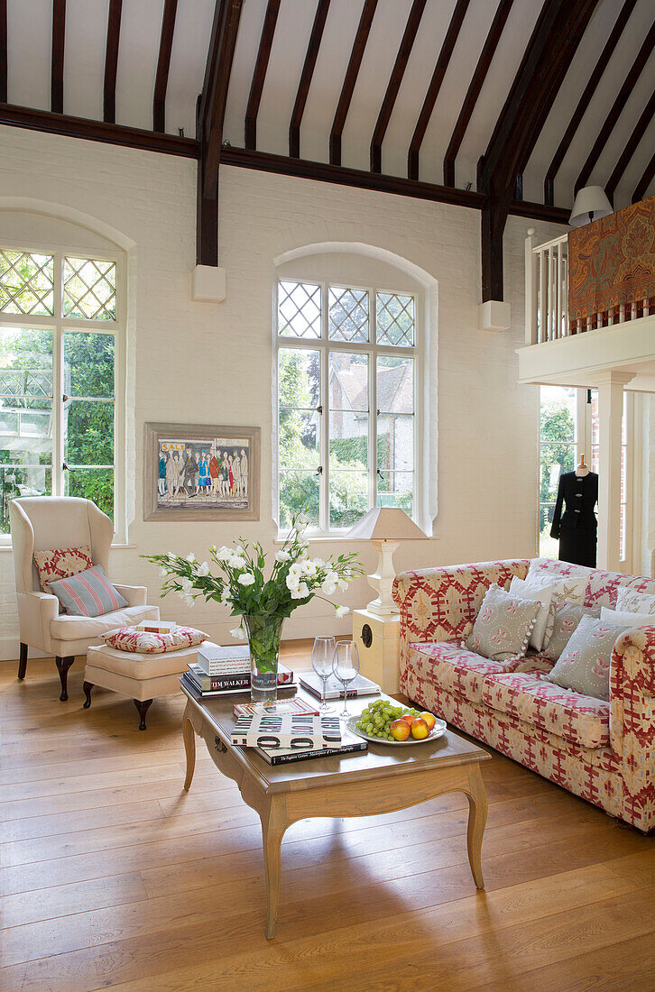 Armchair and footstool with sofa under beamed ceiling in renovated Victorian schoolhouse West Sussex England UK