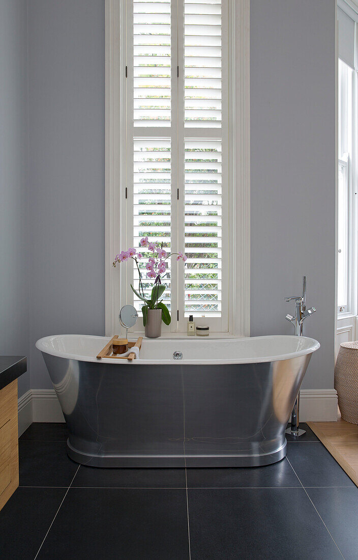 Freestanding silver bath with orchid in window of London townhouse UK