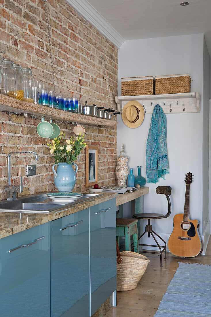 Guitar and desk with saucepans on shelf in exposed brick kitchen of Sussex beach house England UK