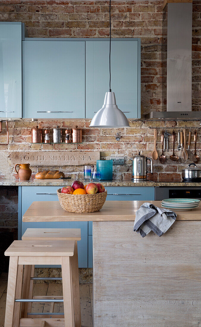 Stainless pendant above fruit basket in teal and exposed brick fitted kitchen in Sussex beach house England UK