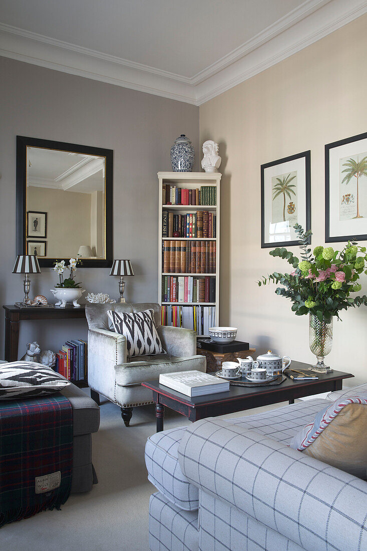Grauer Sessel und Bücherregal mit gerahmten Drucken und Schnittblumen in einer Wohnung in einem Londoner Stadthaus, UK
