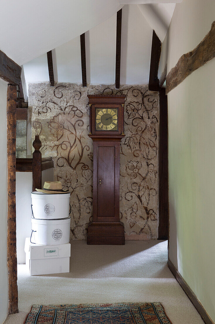 Antique grandfather clock and hat boxes on landing of timber framed Kent farmhouse UK