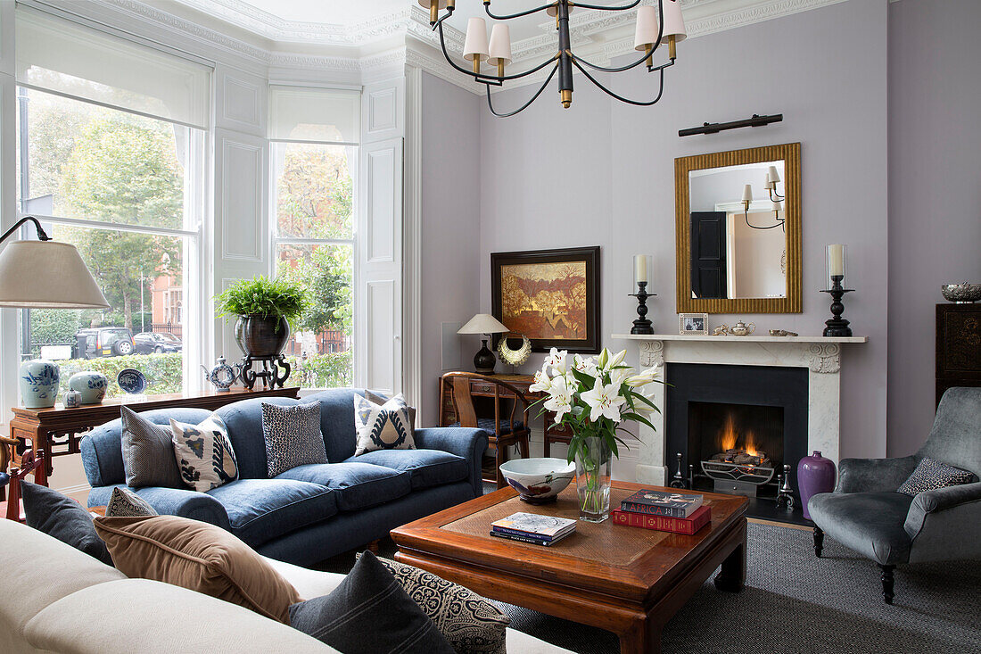 Lilies on wooden coffee table with Vietnamese landscape and lit fire in living room of London townhouse UK