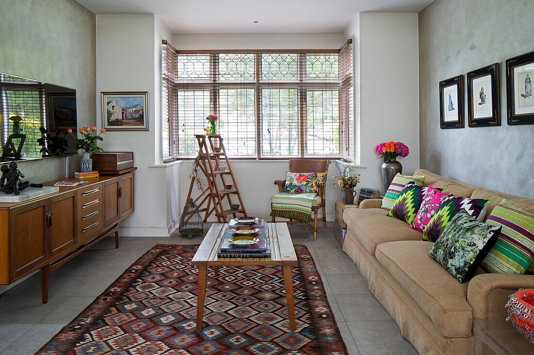 Wooden sideboard and step ladder with bright scatter cushions on sofa in London living room England UK