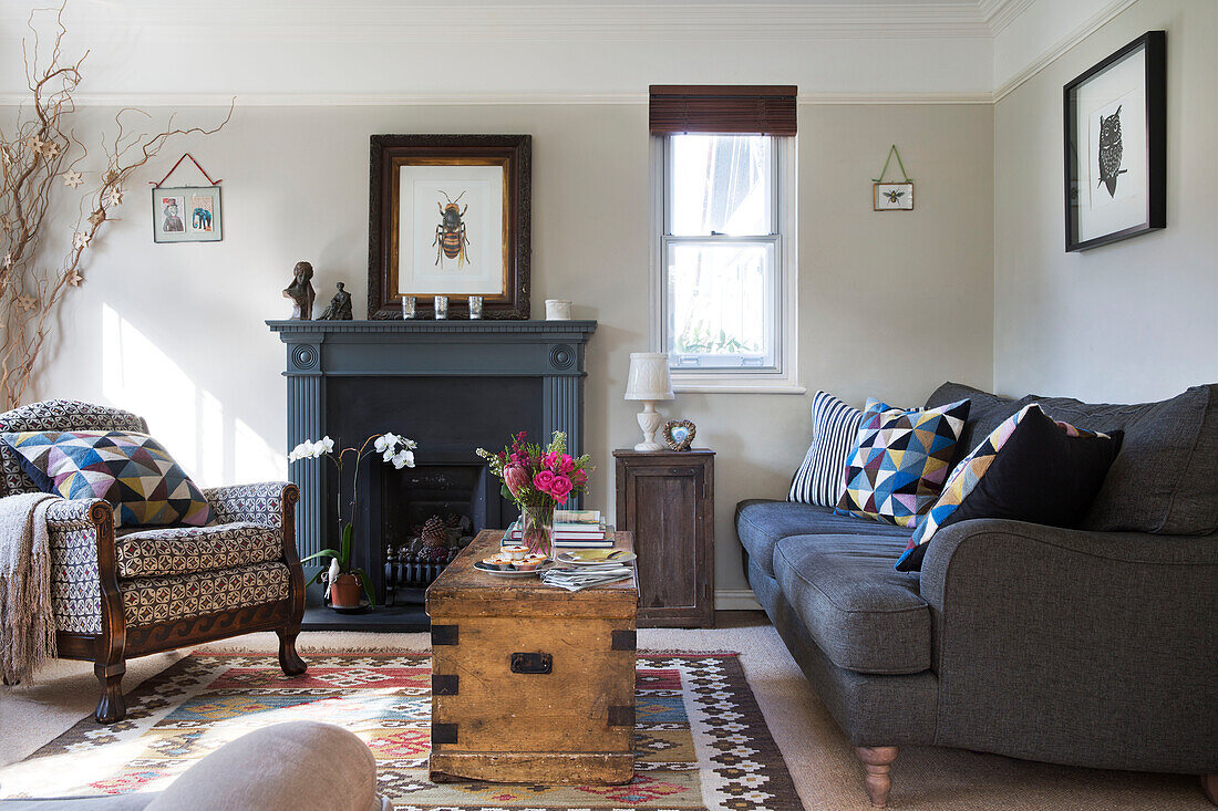 Graues Sofa und Kamin mit Holztruhe und gepolstertem Sessel im Wohnzimmer in Sussex England UK