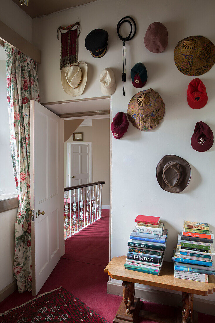 Collection of hats with stacked books on side table and pink carpet on landing in Kelso home Scotland UK