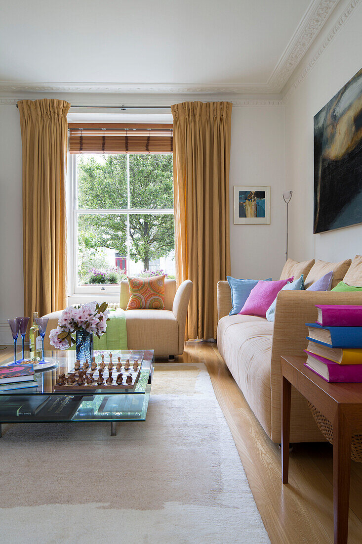 Schachbrett auf niedrigem Glas-Couchtisch mit beigen Sofas in Londoner Stadthaus-Wohnzimmer England UK