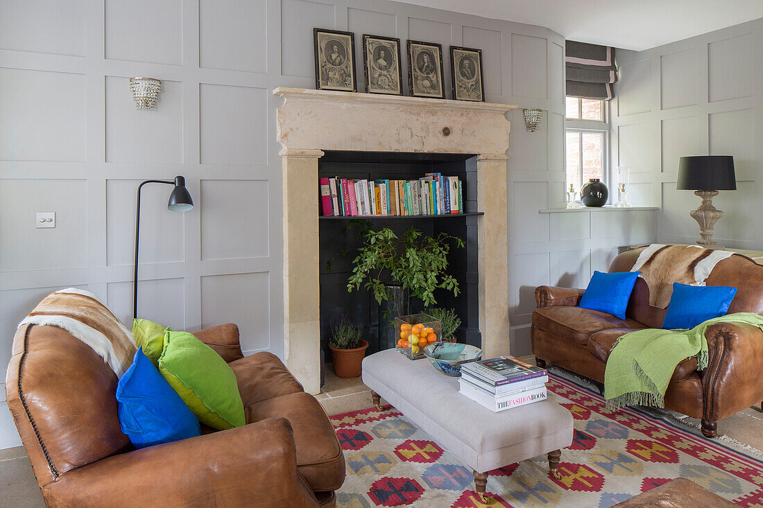 Fireplace repurposed as bookshelf with brown leather two-seater sofas in Gloucestershire living room England UK