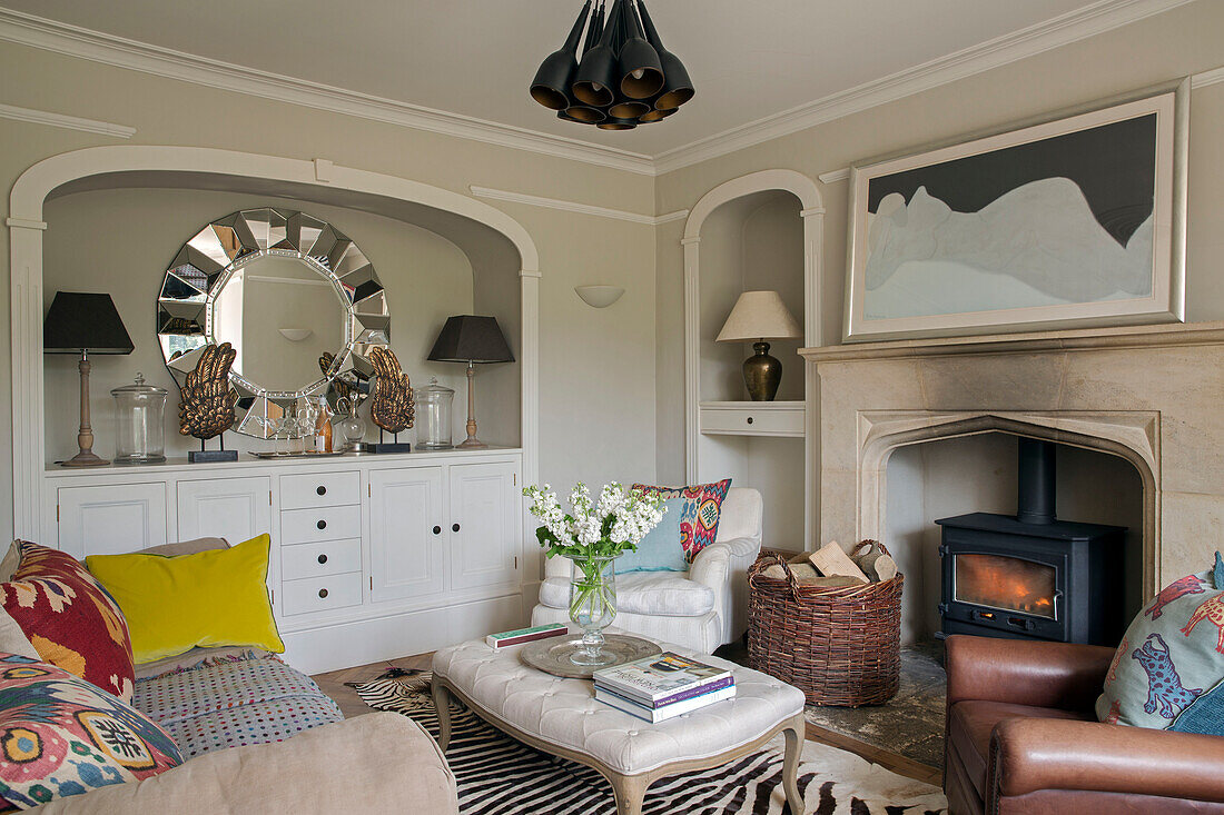 Eingelassener Spiegel und Sideboard im Wohnzimmer mit beleuchtetem Kamin in einem Haus in Gloucestershire England UK