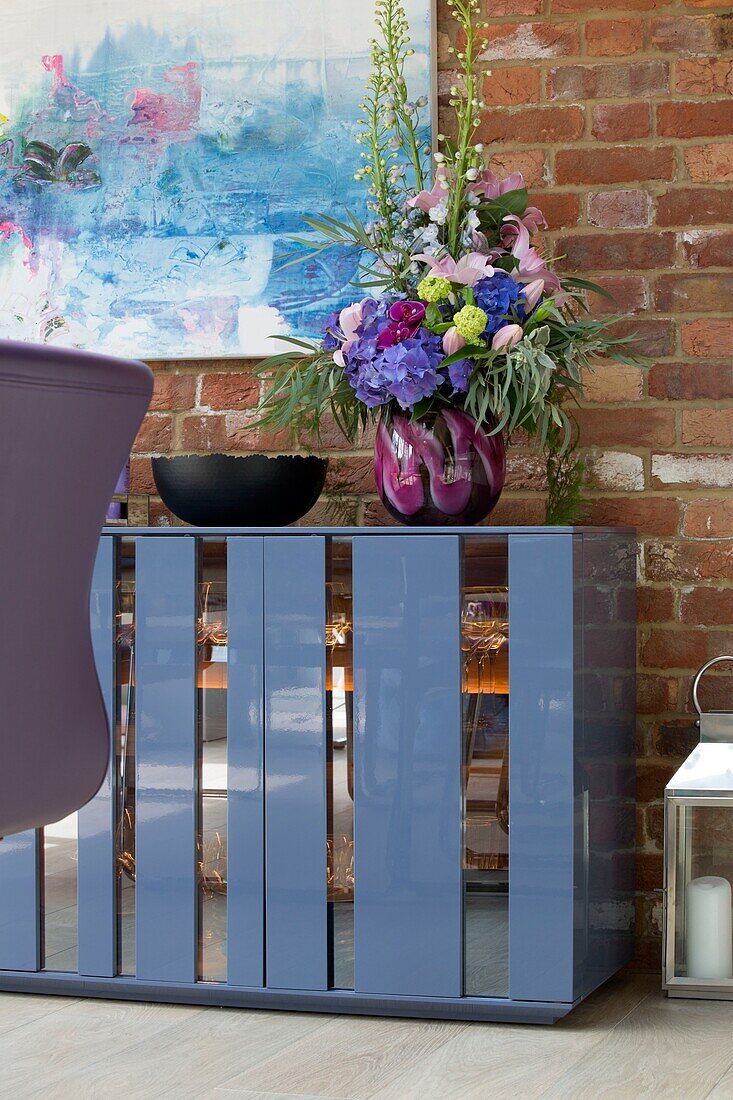 Gläser und Geschirr in blauem Sideboard mit freiliegender Ziegelwand in einem Haus in Sussex, England, UK