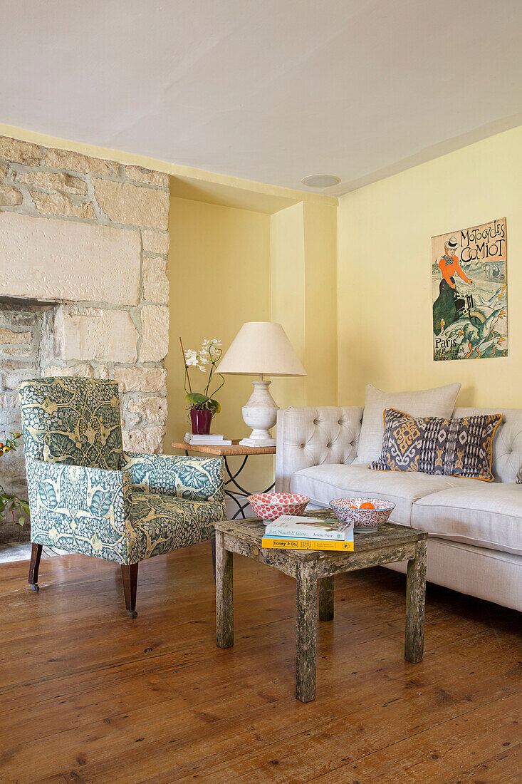 Upholstered armchair with square table and wooden floor in Gloucestershire farmhouse England UK