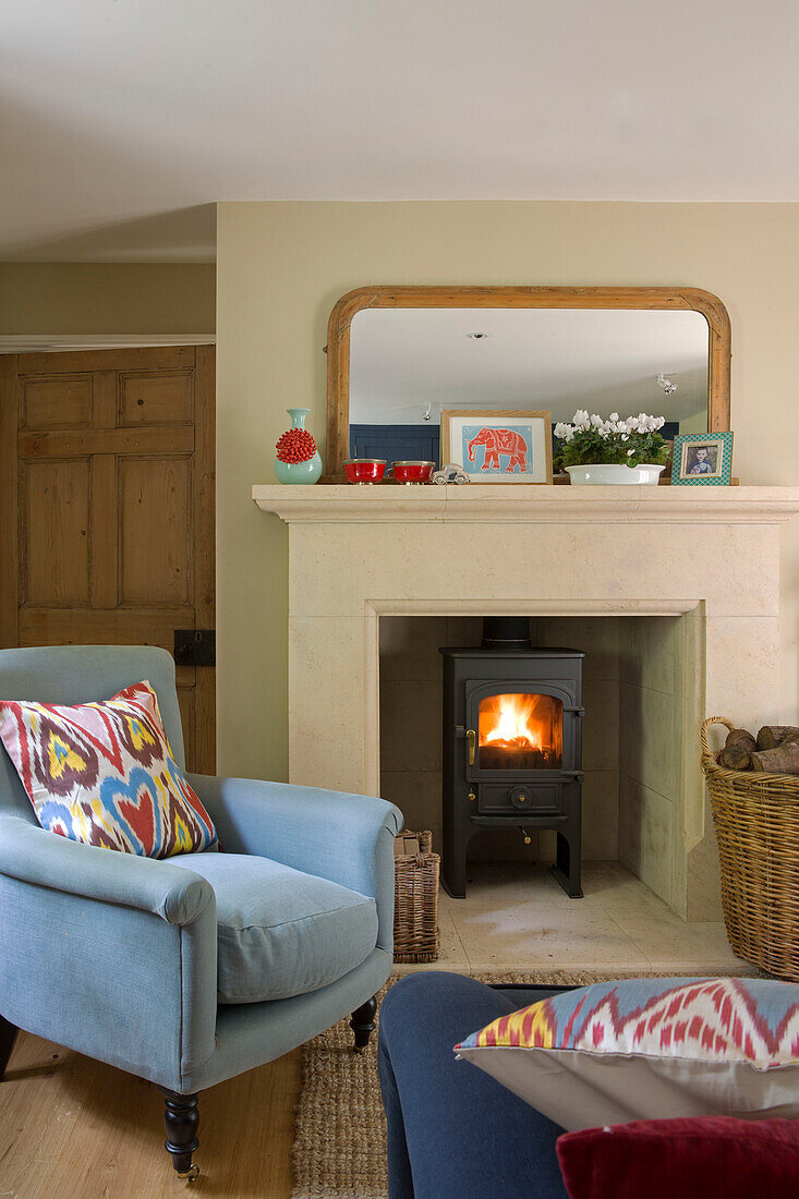 Hellblauer Sessel mit beleuchtetem Holzofen in einem Cottage in Gloucestershire, Großbritannien