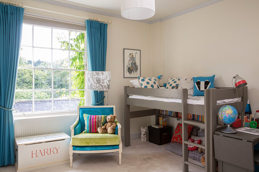 Sessel und Podestbett mit blauen Vorhängen am Fenster in einem freistehenden Landhaus in Sussex UK