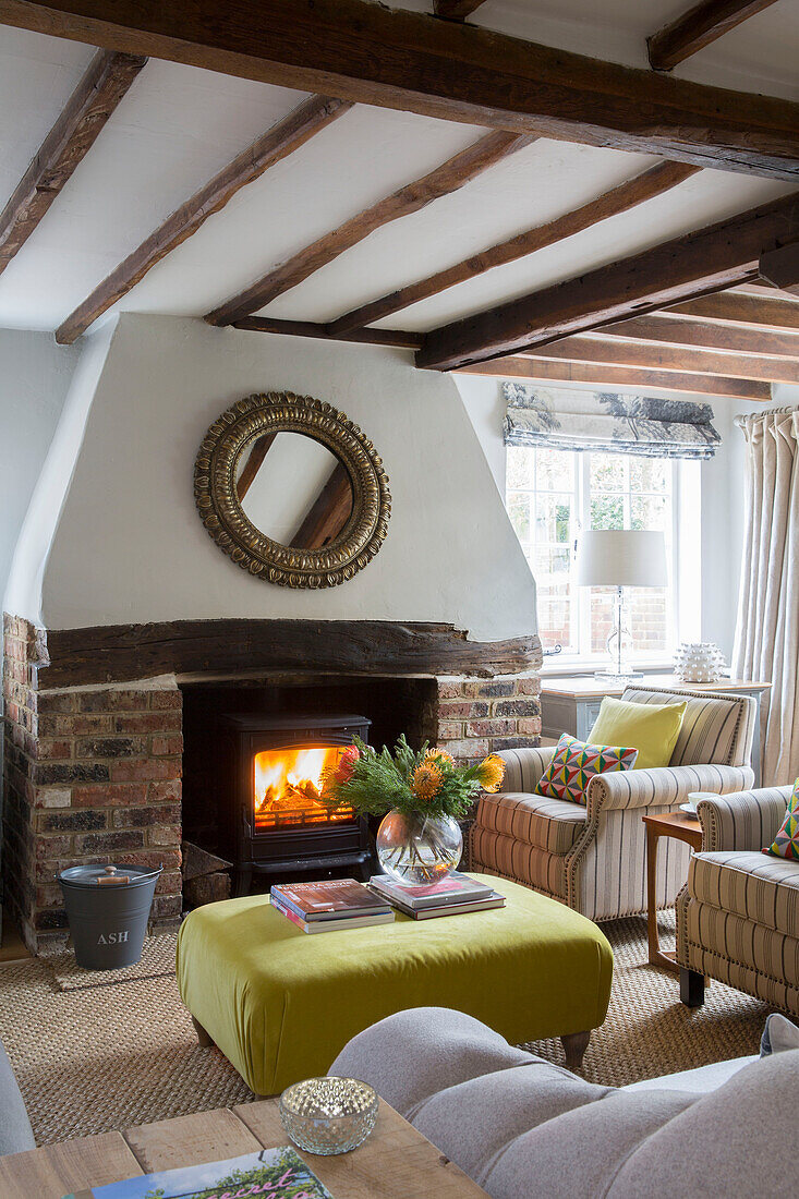 Cut flowers on yellow ottoman with lit woodburner in Oast house conversion Kent UK