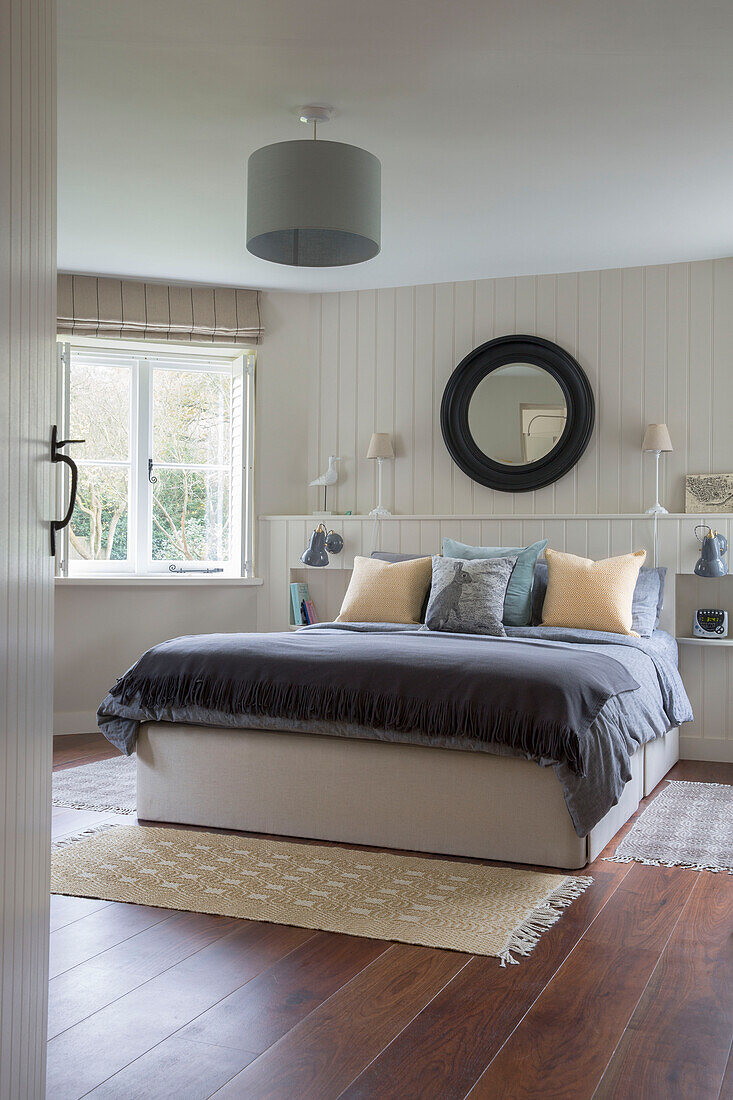 Black circular mirror above double bed below grey lamp in Oast house conversion Kent UK