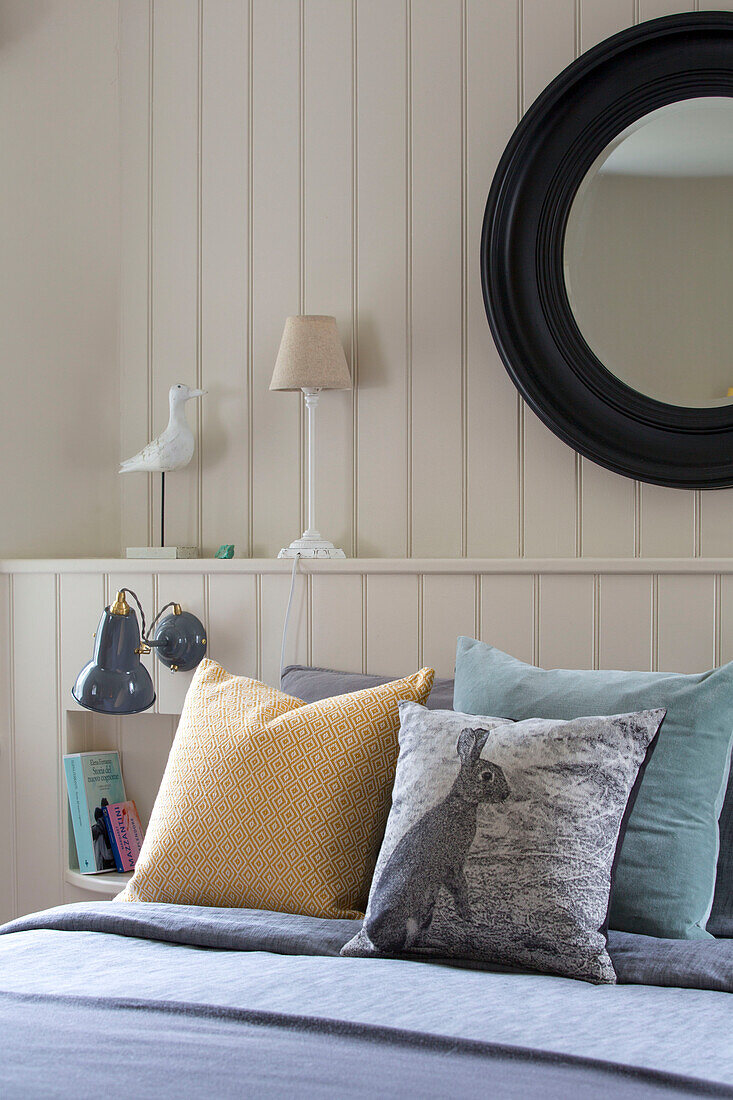 Black circular mirror on panelled wall above double bed in Oast house conversion Kent UK