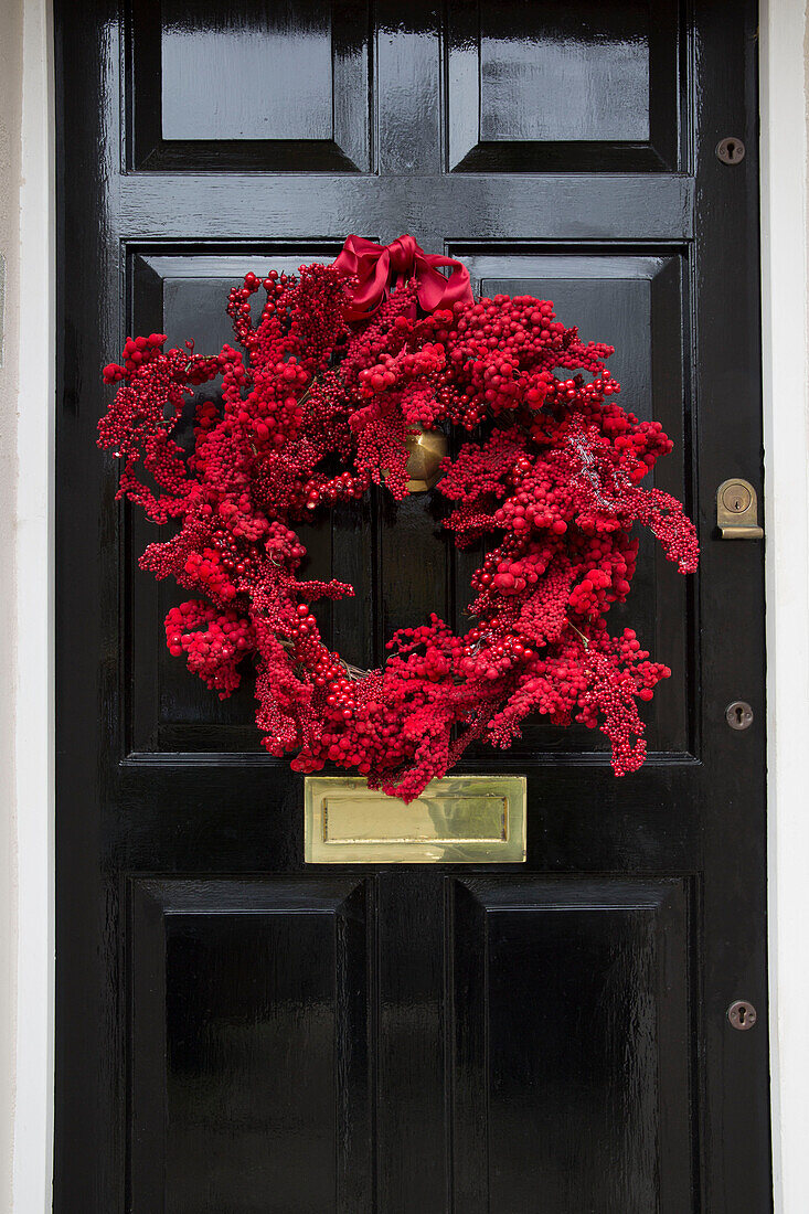 Kranz aus roten Beeren an schwarzer Haustür eines Londoner Stadthauses UK