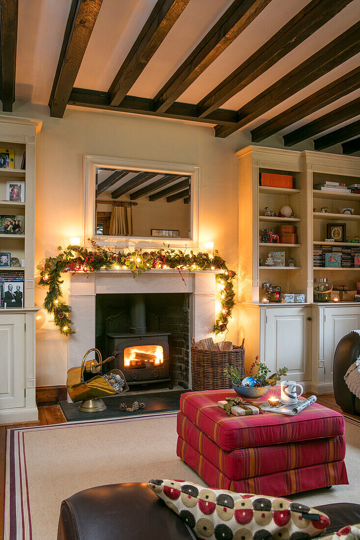 Lit woodburning stove with fairylit garland and pink ottoman footstool in Berkshire home UK