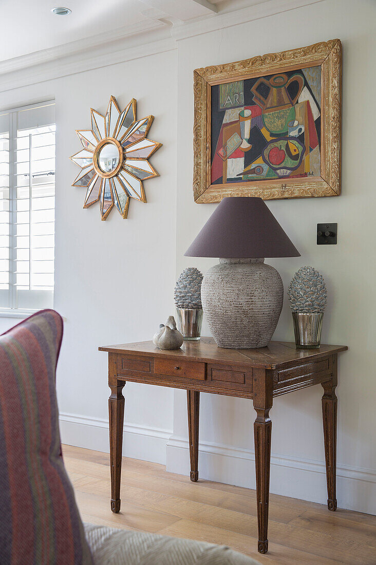 Lamp and ornaments on wooden table with artwork and mirror in West Sussex home