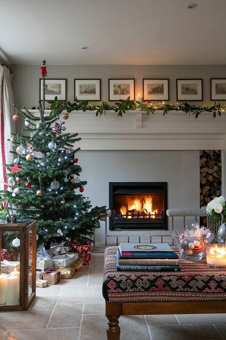 Weihnachtsbaum mit Geschenken und beleuchtetem Feuer im Wohnzimmer eines Bauernhauses in Dorset UK