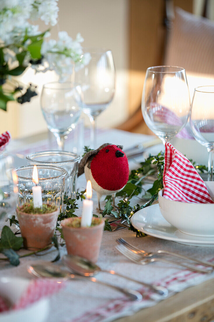 Gingham-Serviette und rotes Rotkehlchen mit brennenden Kerzen auf dem Esstisch in einem Bauernhaus in West Sussex, England