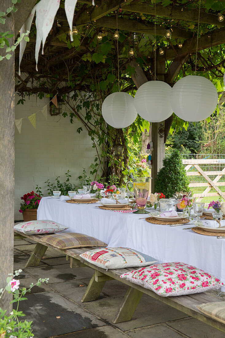 Paper shades hang from pergola over dining table with seat cushions in Alford garden Surrey UK