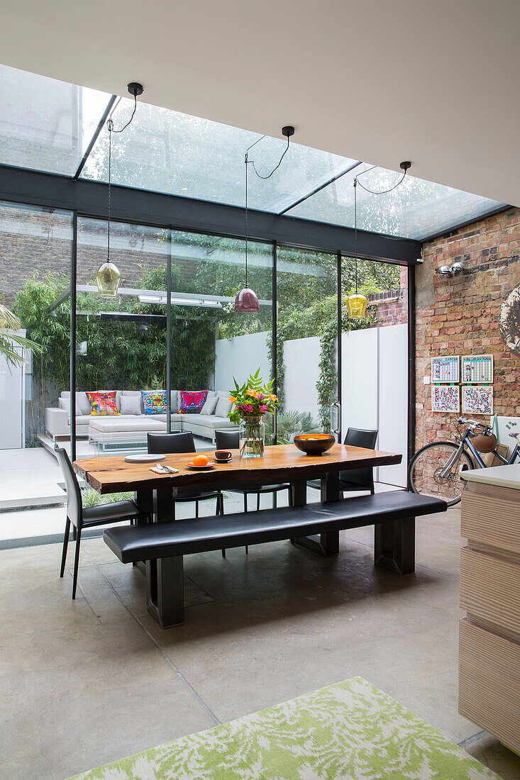 Table and bench seats with exposed brick wall in glass extension of Victorian London townhouse UK