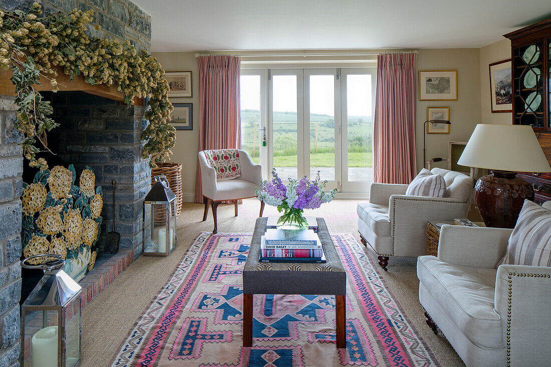 Flower garland above stone fireplace with ottoman and white seating in living room of Somerset farmhouse UK