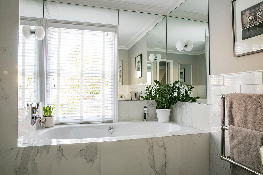 Marble bath with houseplant and corner mirror below window in London home UK