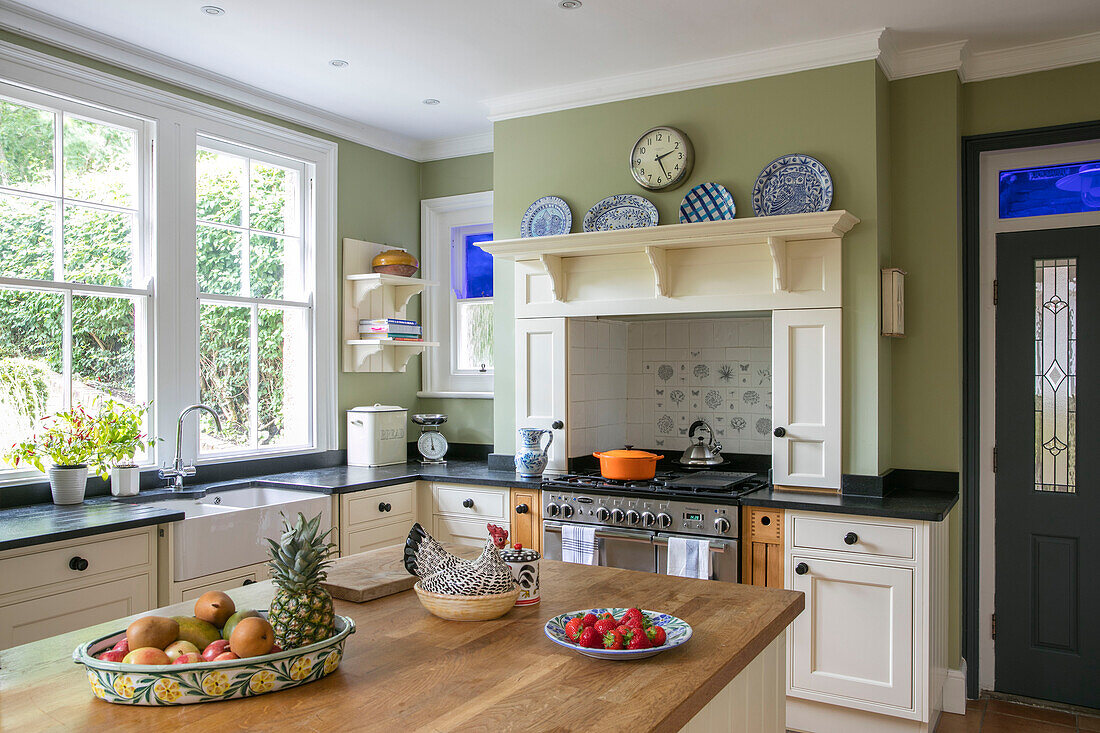 Decorative plates above recessed stove with fruit on worktop at window of terraced Arts and Crafts home Sevenoaks Kent UK