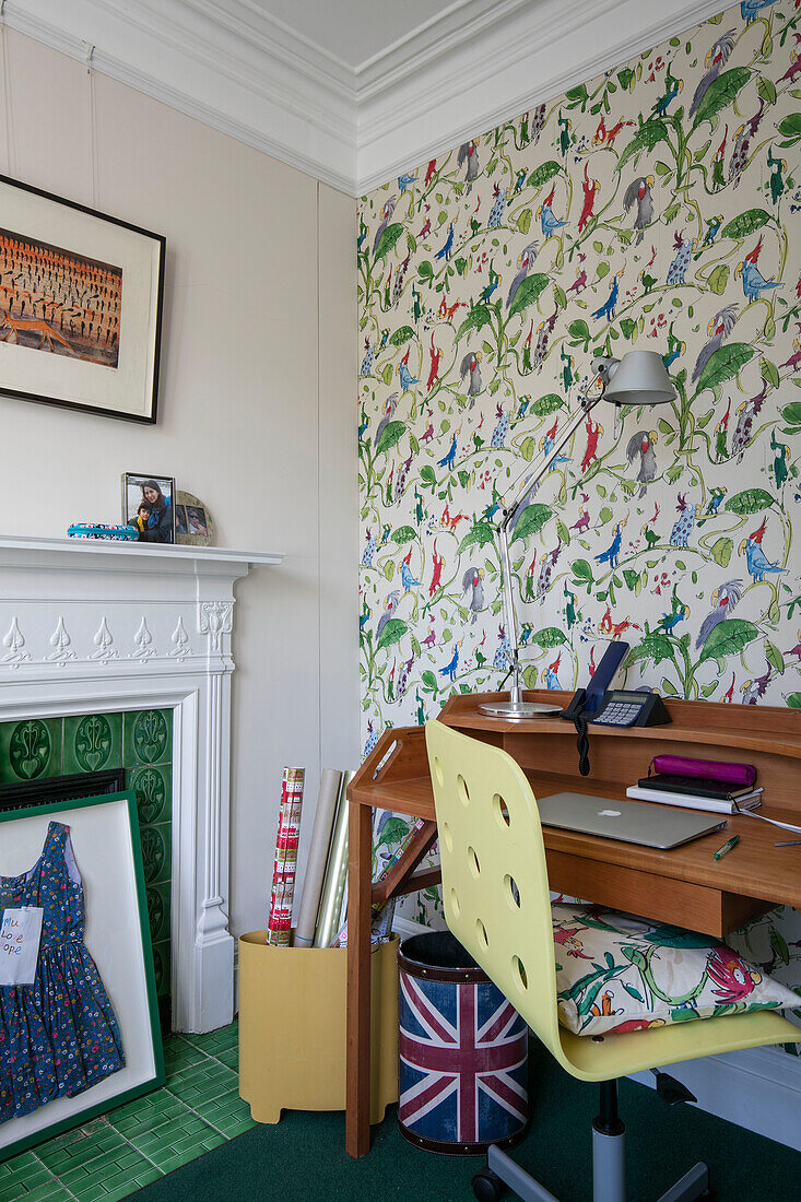 Desk and chair at green tiled fireplace with patterned wallpaper in terraced house Sevenoaks Kent UK