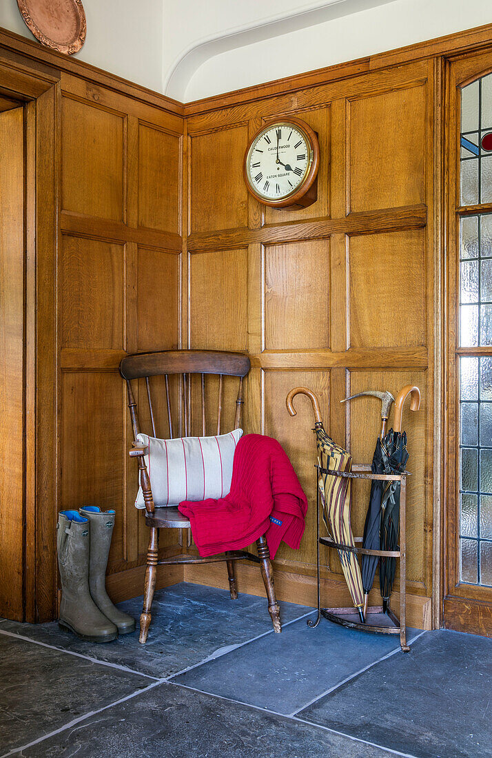 Wooden chair and wellington boots in panelled hallway of Devon home UK