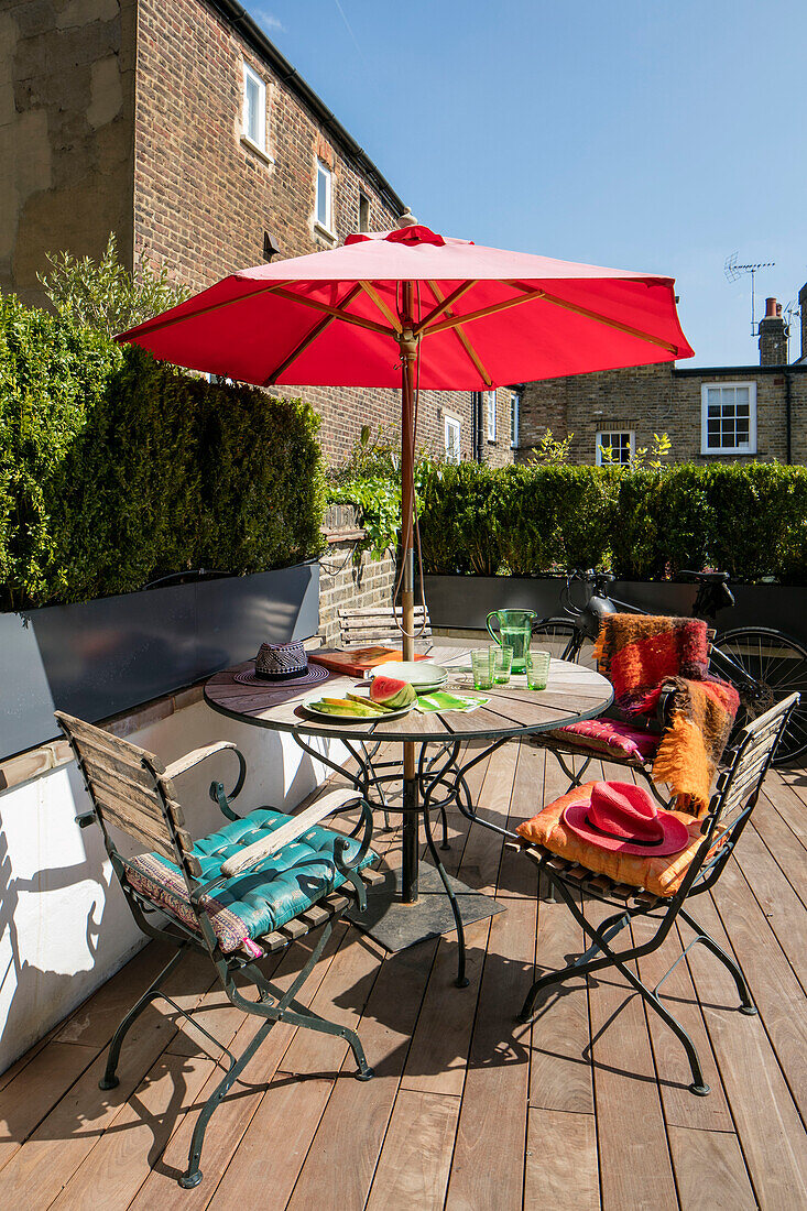 Garden furniture on decking of North London Victorian terrace with red parasol UK