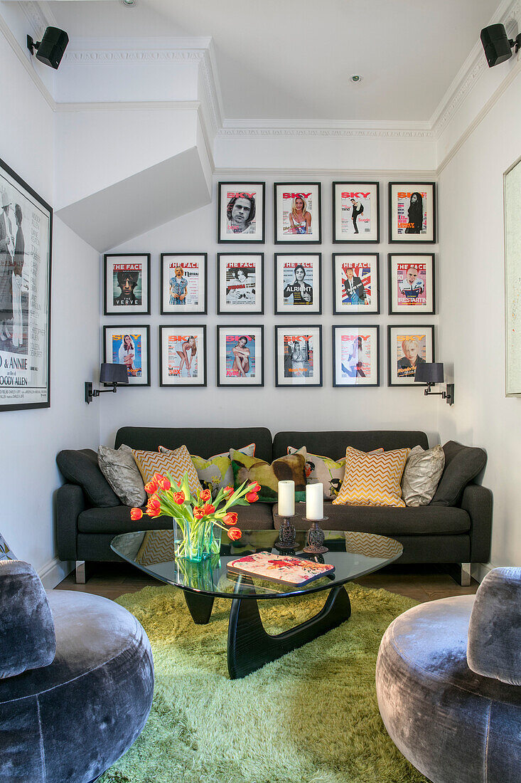 Picture wall of posters above grey sofa with glass topped coffee table in North London home UK
