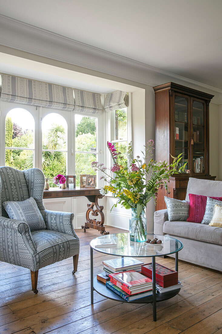 Cut flowers on glass table with wingback armchair in Kent cottage UK