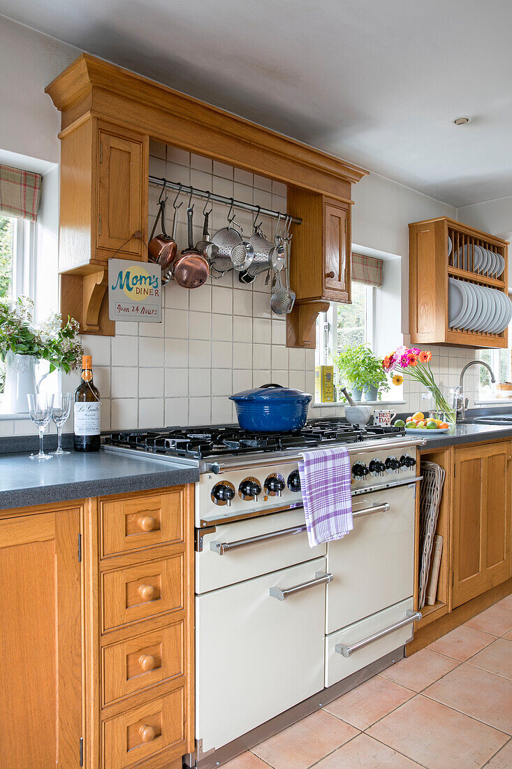 Blue casserole on hob in wooden kitchen with pan and plate racks Kent UK