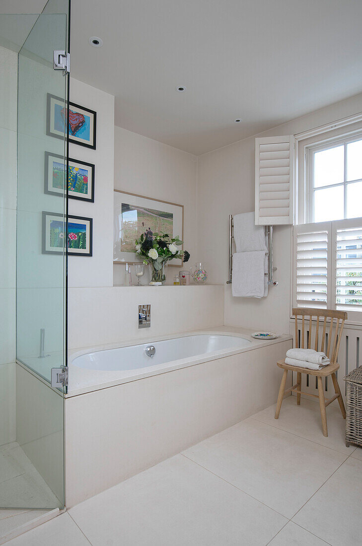 Glass screen and bath with shutters at window in London home UK