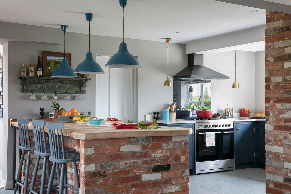 Pendant lights hang above exposed brick worktop in open plan kitchen Hampshire England UK