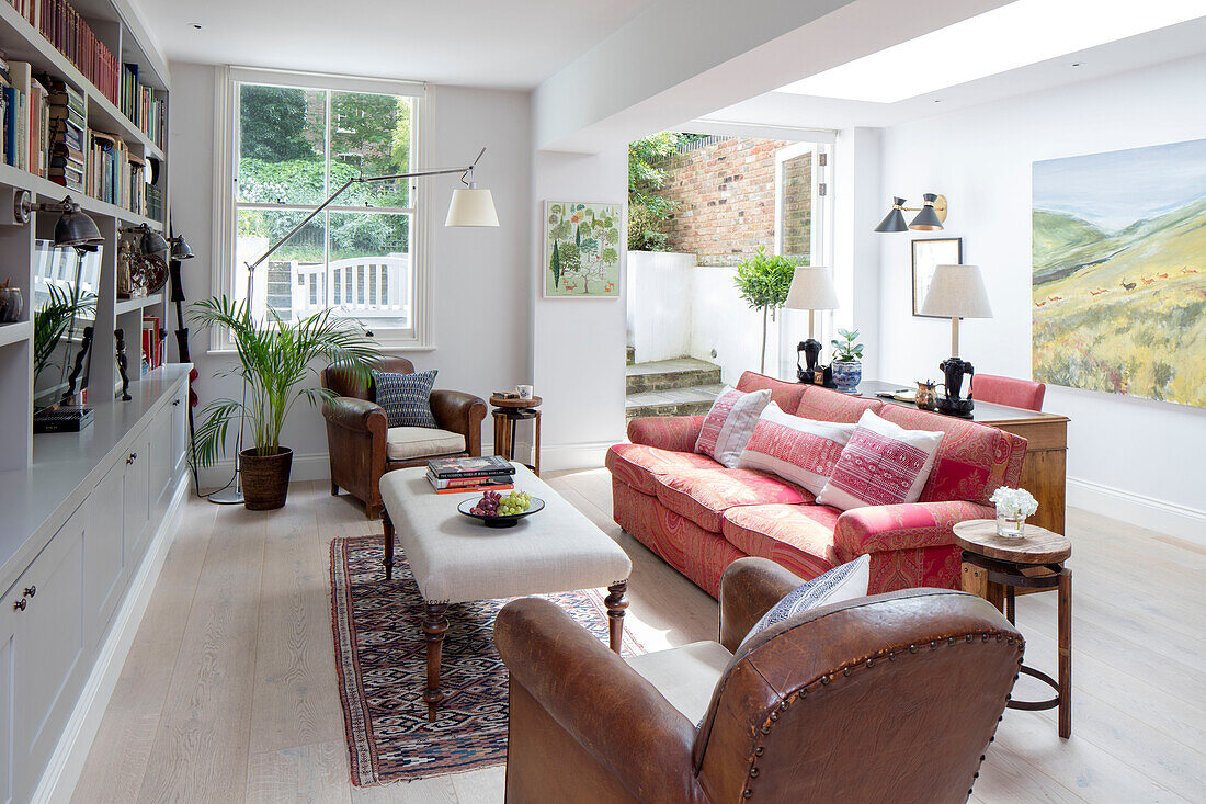 Red sofa with ottoman and wall shelving in basement extension of North London apartment UK