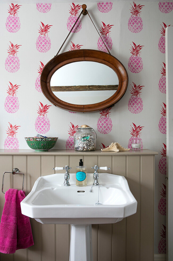 PInk pineapple wallpaper and oval mirror above pedestal basin in Hampshire home England UK